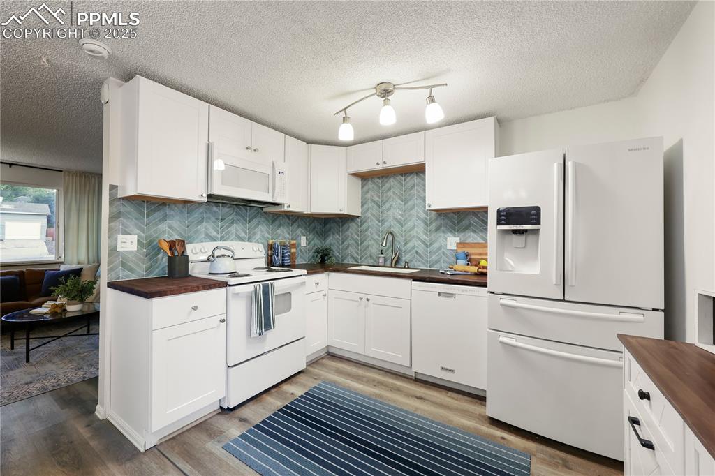 Kitchen with butcher block counters, white appliances, white cabinetry, a textured ceiling, and decorative backsplash