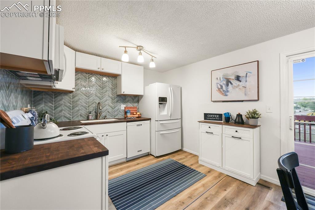 Kitchen featuring butcher block countertops, white cabinets, backsplash, white appliances, and light wood-style floors