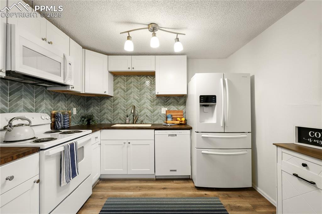 Kitchen with white appliances, tasteful backsplash, white cabinetry, butcher block countertops, and a textured ceiling