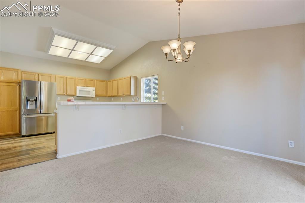 Kitchen with vaulted ceiling, stainless steel fridge with ice dispenser, light carpet, light brown cabinets, and light countertops