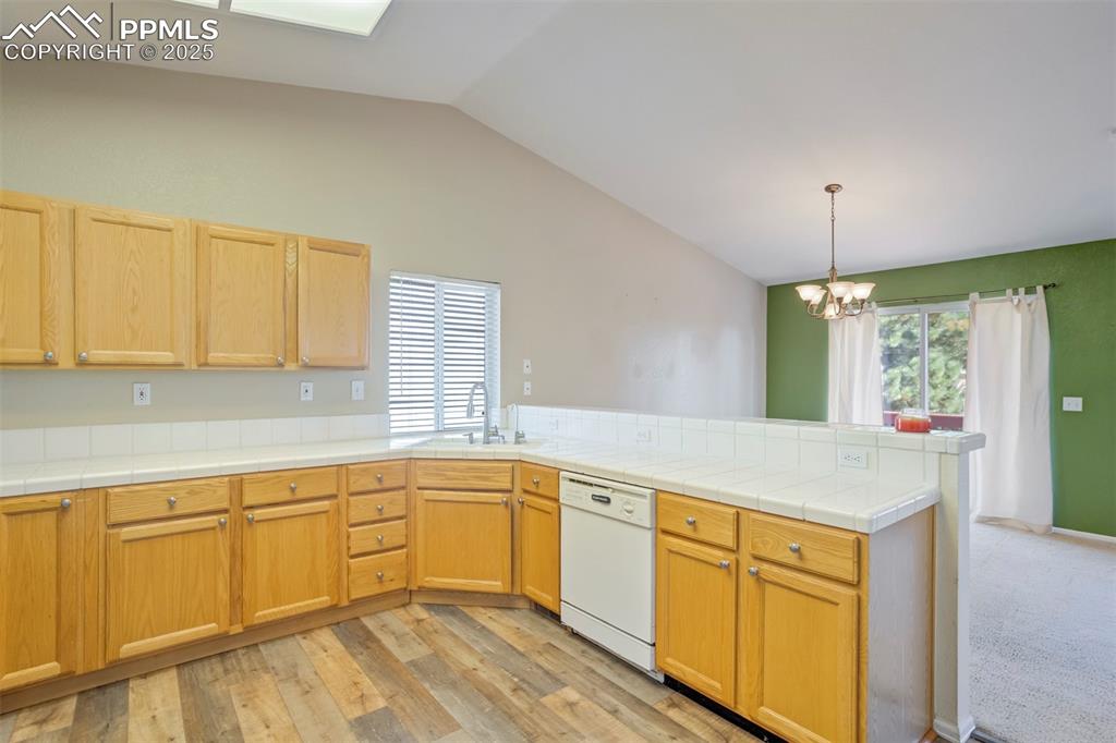 Kitchen with a peninsula, vaulted ceiling, tile countertops, dishwasher, and a chandelier