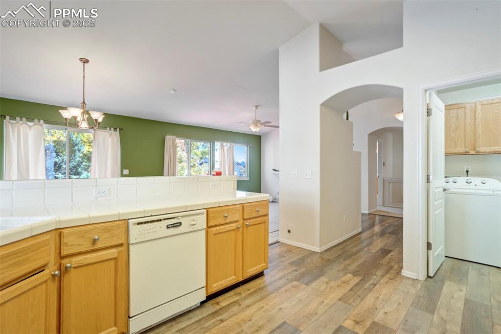 Kitchen featuring washer / dryer, arched walkways, white dishwasher, light wood finished floors, and tile counters