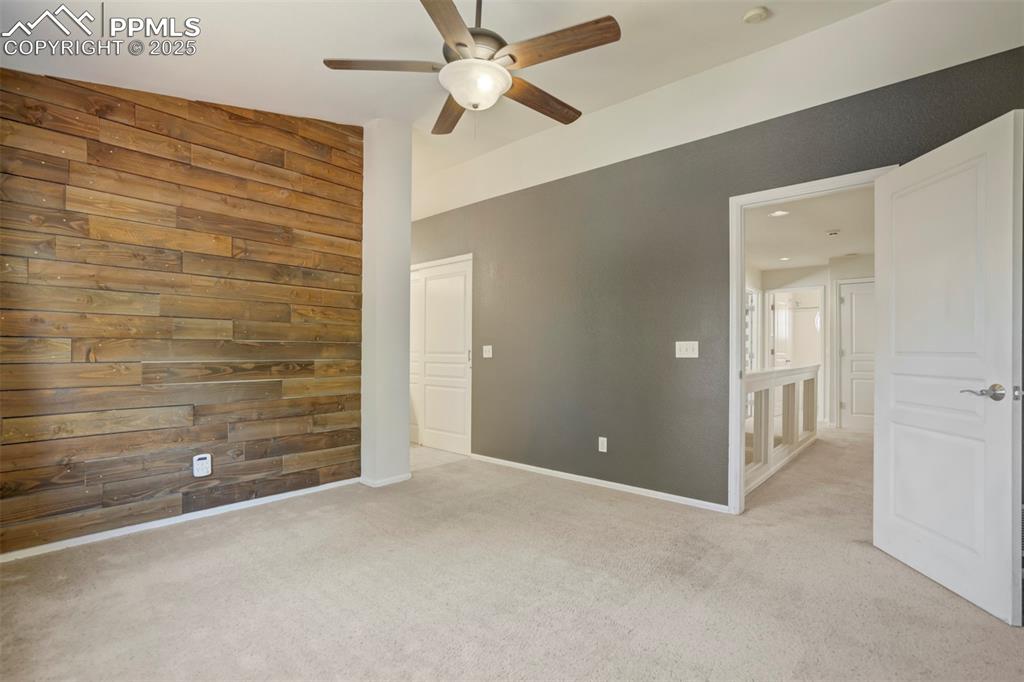 Unfurnished bedroom featuring wooden walls, carpet floors, and a ceiling fan