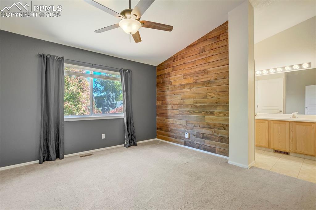 Spare room featuring wooden walls, light colored carpet, vaulted ceiling, an accent wall, and ceiling fan