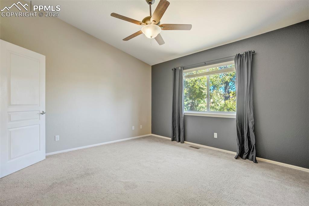 Empty room featuring light carpet, vaulted ceiling, and a ceiling fan