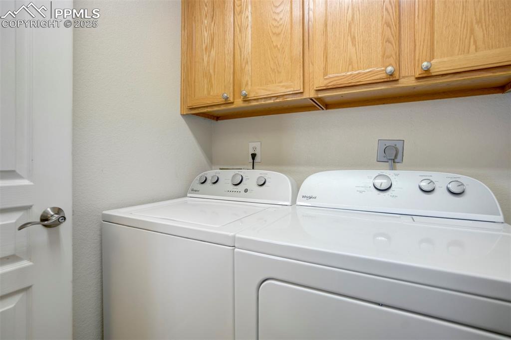 Washroom with cabinet space, washing machine and dryer, and a textured wall