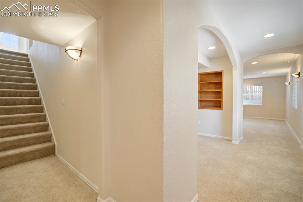 Corridor with light carpet, arched walkways, stairway, and recessed lighting