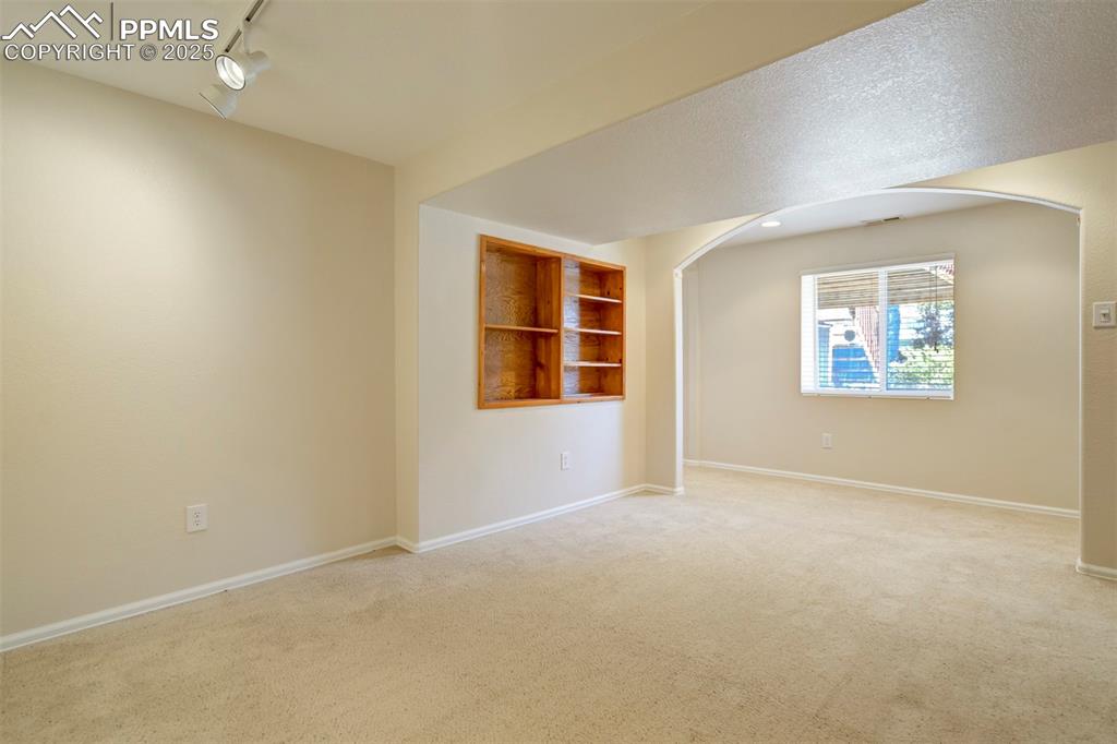 Carpeted empty room featuring track lighting and arched walkways