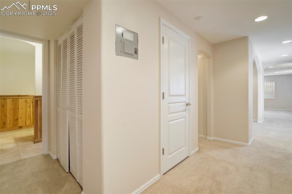 Hallway with arched walkways, light colored carpet, recessed lighting, and electric panel