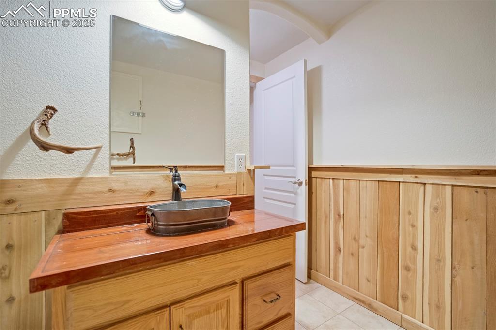 Bathroom featuring wood walls, vanity, light tile patterned flooring, a wainscoted wall, and a textured wall