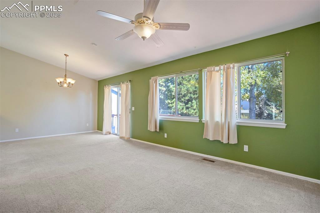 Empty room featuring carpet flooring, a ceiling fan, a chandelier, and vaulted ceiling
