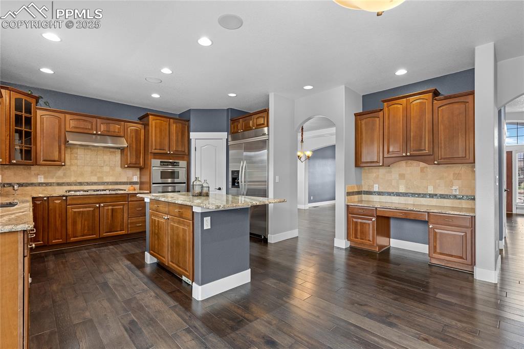 Kitchen with decorative backsplash, arched walkways, brown cabinetry, a center island and recessed lighting