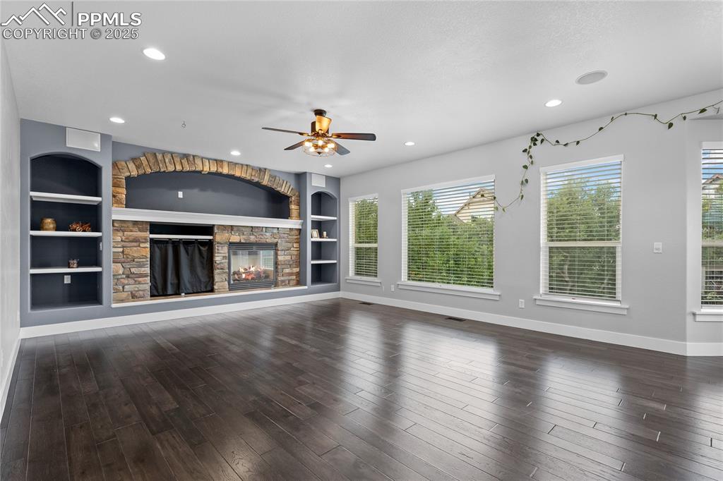  living room with built in features, a stone fireplace, dark wood-type flooring, ceiling fan, and recessed lighting