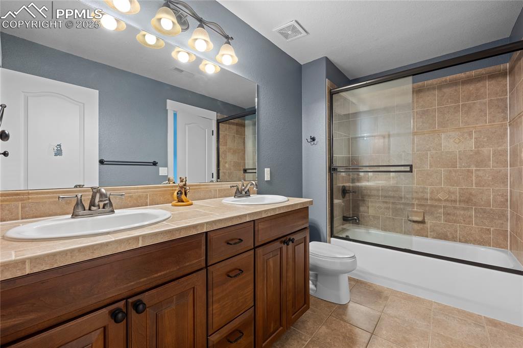 Jack and Jill Bathroom with enclosed tub / shower combo, light tile patterned floors and double vanity.
