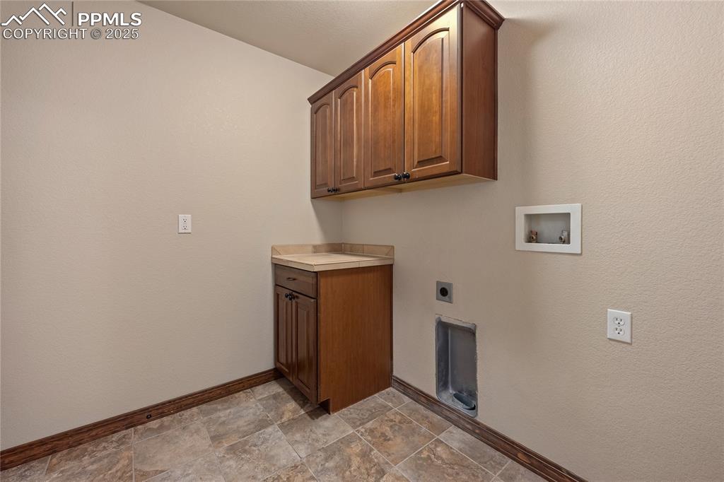 Laundry room featuring cabinet space, electric dryer hookup, hookup for a washing machine and stone finish floors.