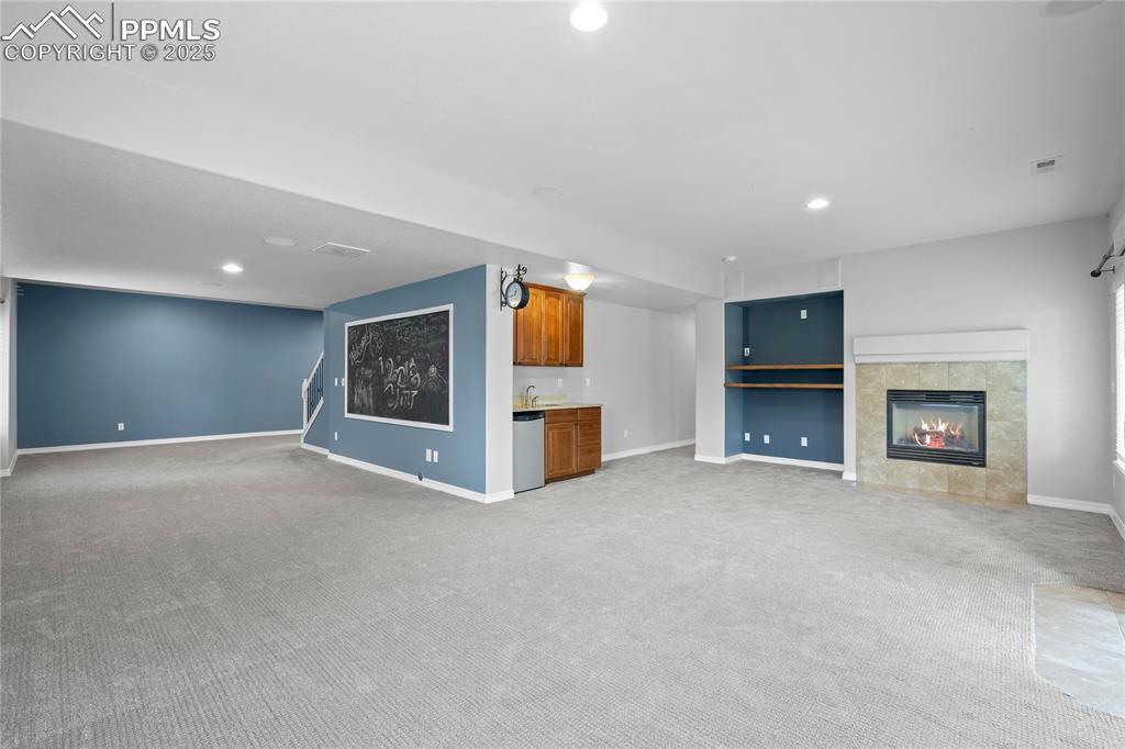 Basement family room featuring a tile fireplace, recessed lighting, wet bar, and light colored carpet