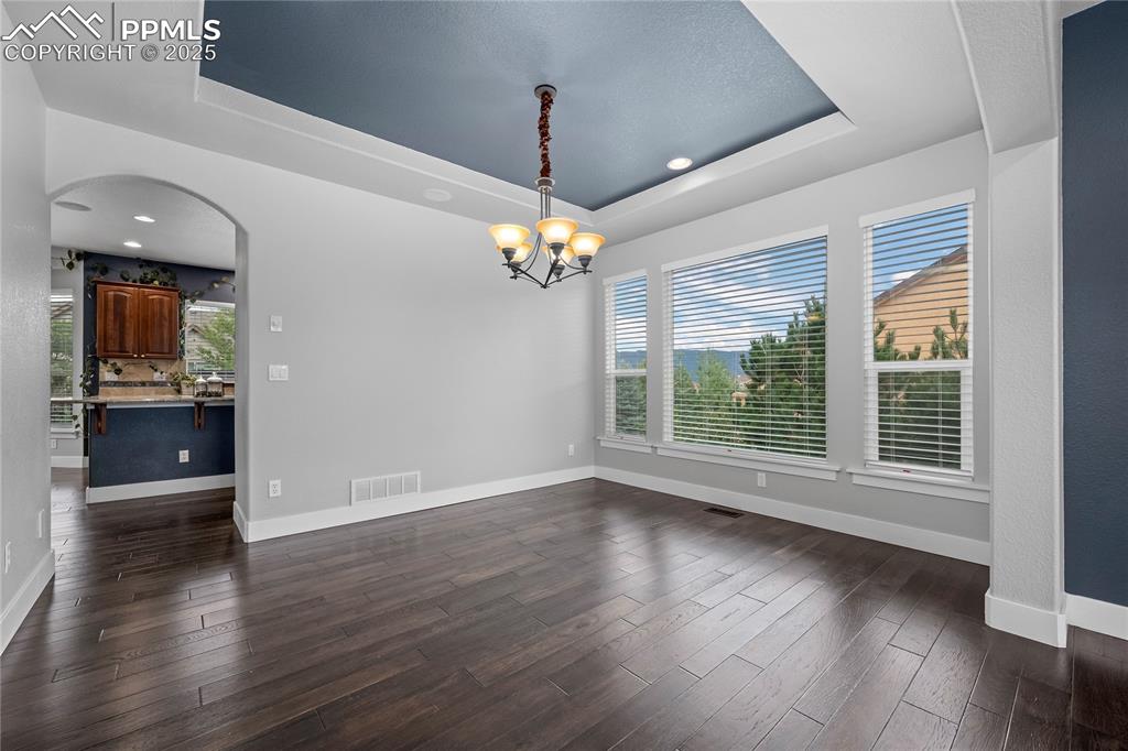 Dining area featuring a tray ceiling, dark wood-style floors, arched walkways, and a chandelier