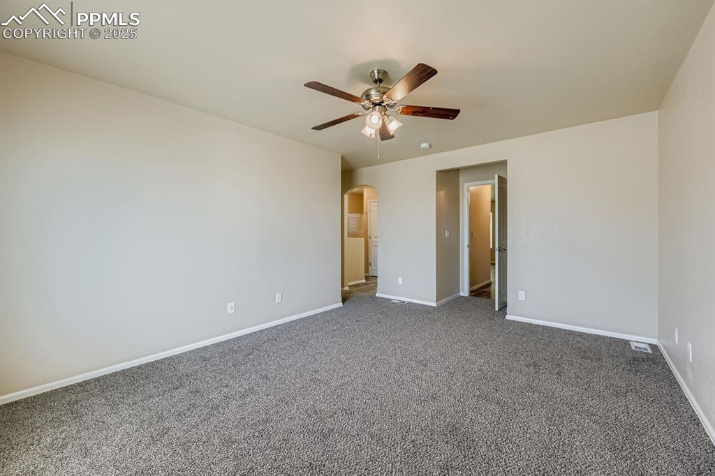 Unfurnished bedroom with arched walkways, a ceiling fan, and carpet