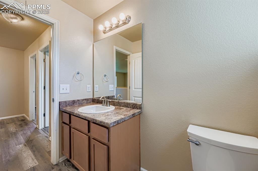 Half bath featuring a textured wall, vanity, and dark wood finished floors
