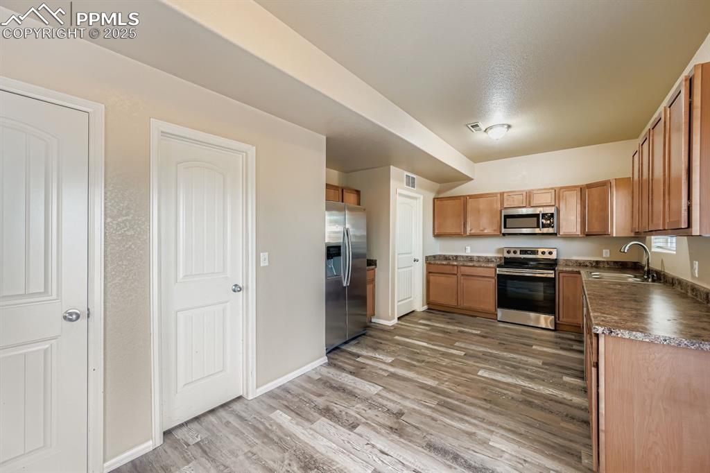 Kitchen featuring dark countertops, appliances with stainless steel finishes, light wood-style floors, and brown cabinets