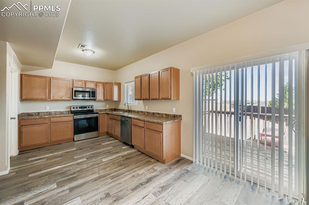 Kitchen with stainless steel appliances, light wood finished floors, dark countertops, and brown cabinetry