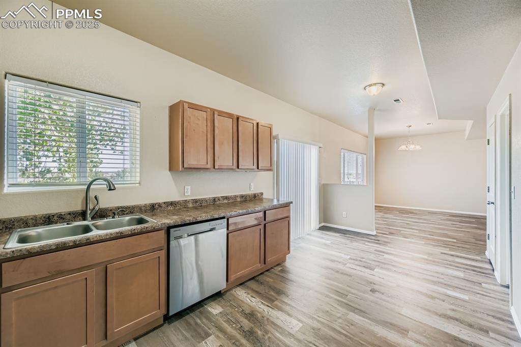 Kitchen with dark countertops, healthy amount of natural light, dishwasher, light wood finished floors, and a textured ceiling