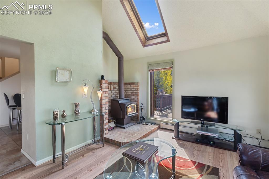 Living room featuring a wood stove, lofted ceiling, a skylight, and wood finished floors
