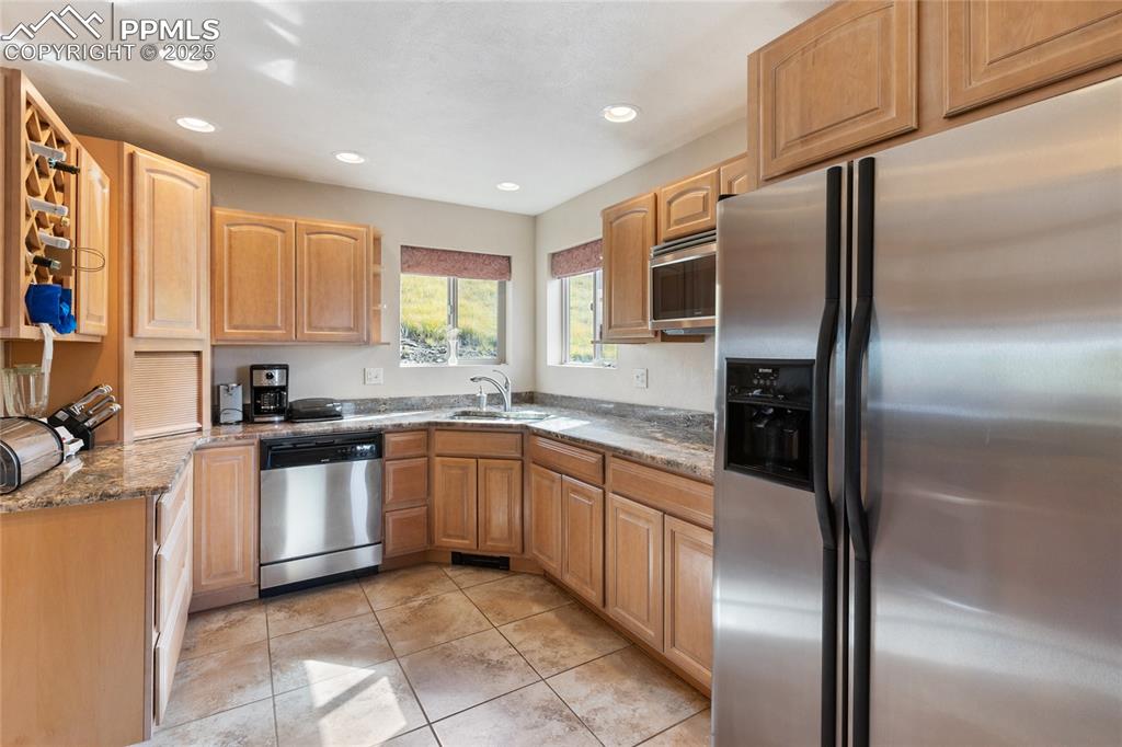 Kitchen with appliances with stainless steel finishes, light stone counters, recessed lighting, light tile patterned floors, and light brown cabinetry