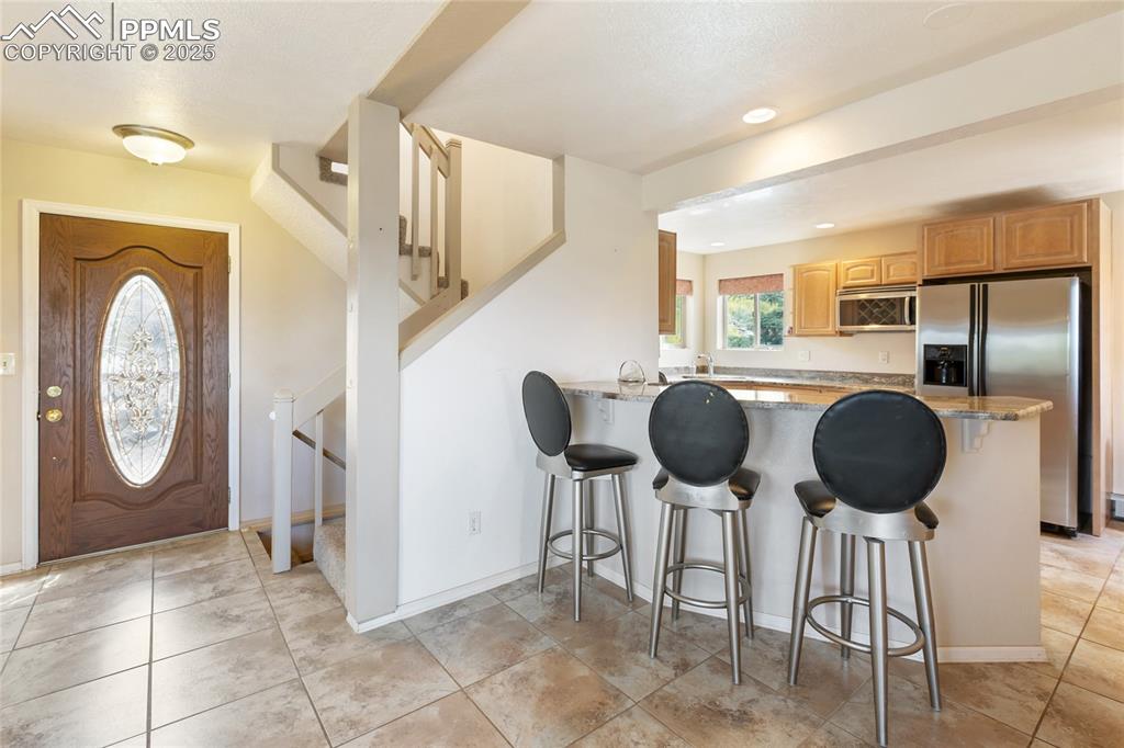 Kitchen featuring a breakfast bar area, appliances with stainless steel finishes, a peninsula, light stone counters, and light tile patterned flooring