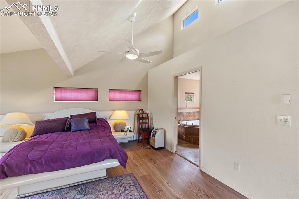 Bedroom featuring connected bathroom, wood finished floors, a ceiling fan, high vaulted ceiling, and beam ceiling