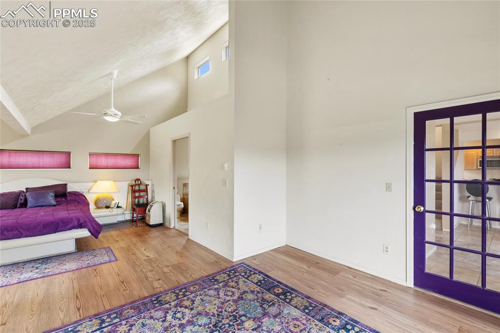 Bedroom with high vaulted ceiling, light wood-style floors, ensuite bathroom, and ceiling fan