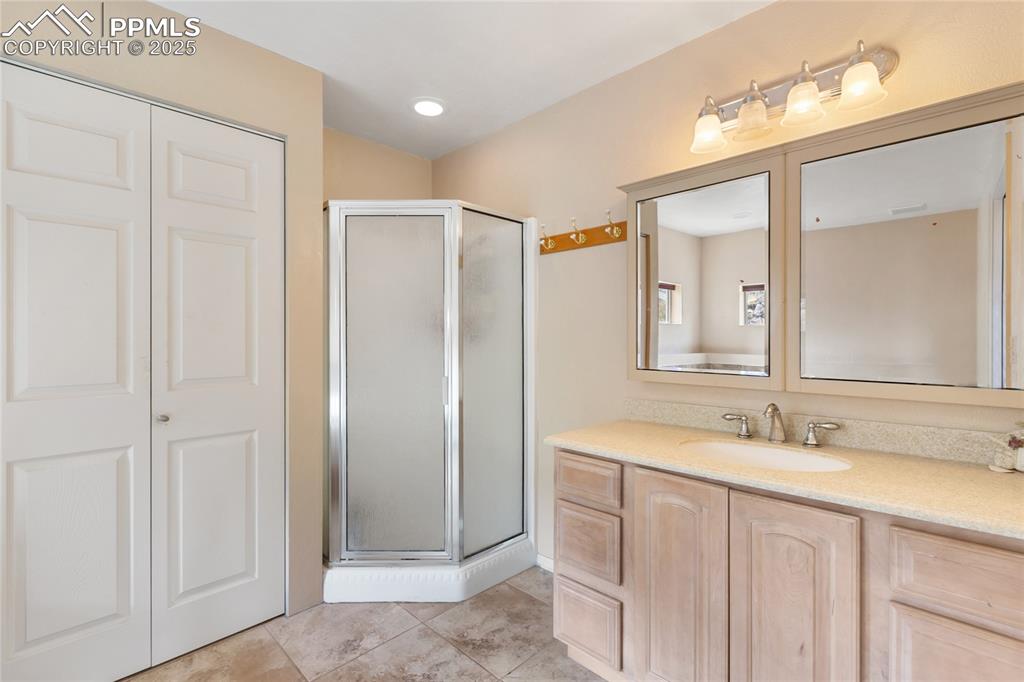 Full bath with a shower stall, vanity, a closet, and light tile patterned floors