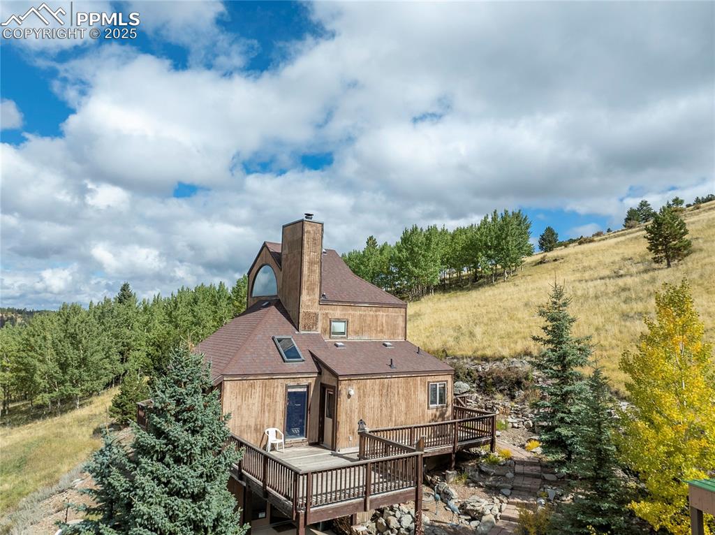 Rear view of house featuring a chimney, a deck, and a shingled roof