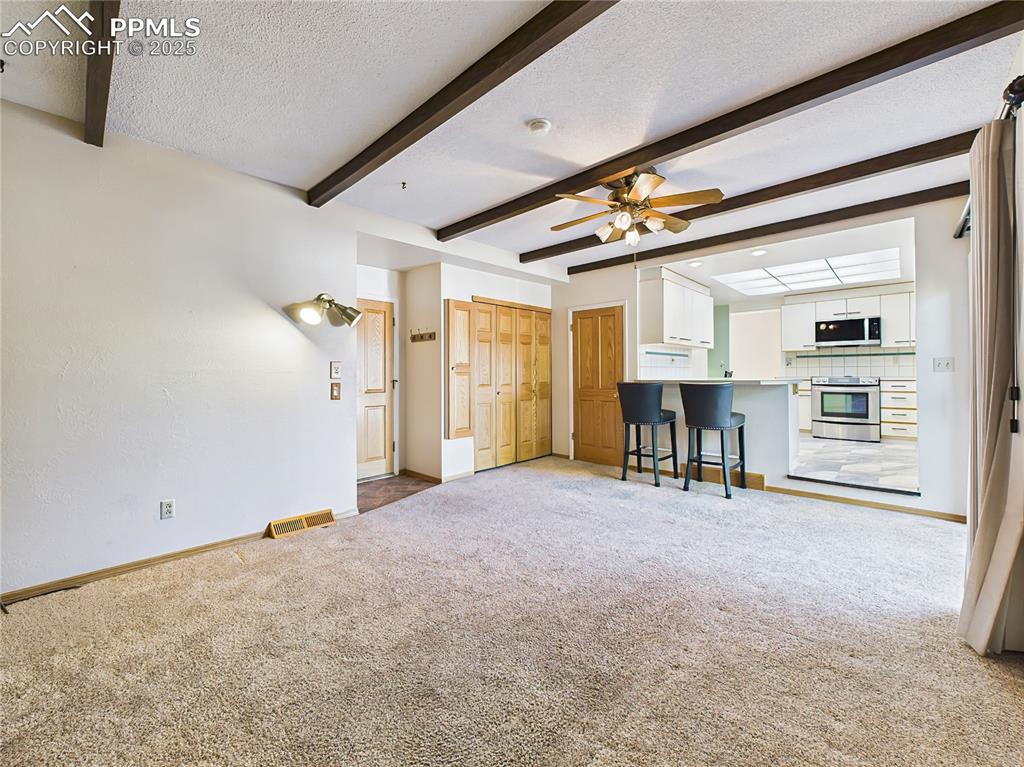 Family Room Toward Kitchen (Empty) – This comfortable family room offers exposed beams, plush carpet, and a seamless connection to the kitchen and outdoor deck—ideal for entertaining or relaxing.