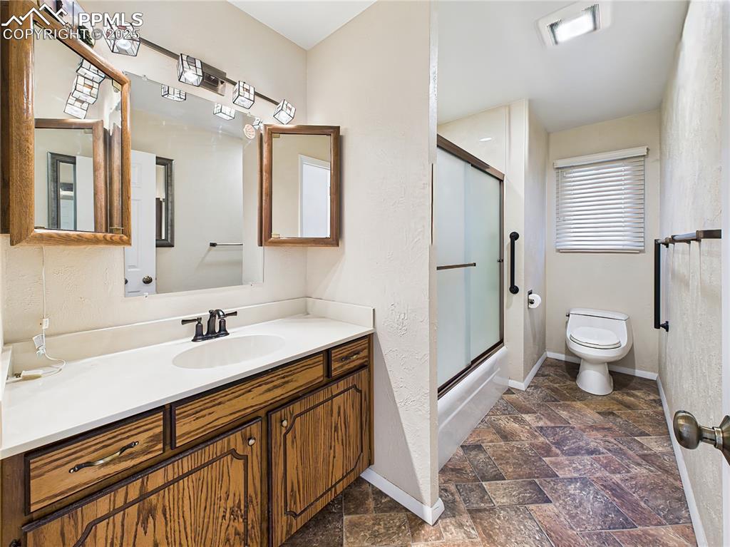 Main Level Guest Bathroom – Well-maintained full bath featuring updated flooring (2023), a spacious vanity with dual medicine cabinets, and a tub/shower combo with sliding glass doors and grab bars for added accessibility.