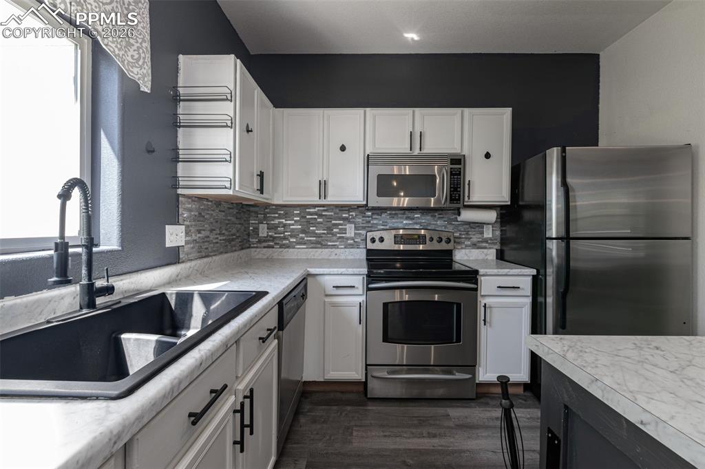 Two tone kitchen featuring two tone cabinetry, stainless steel appliances, light countertops, decorative backsplash, and dark wood-type flooring