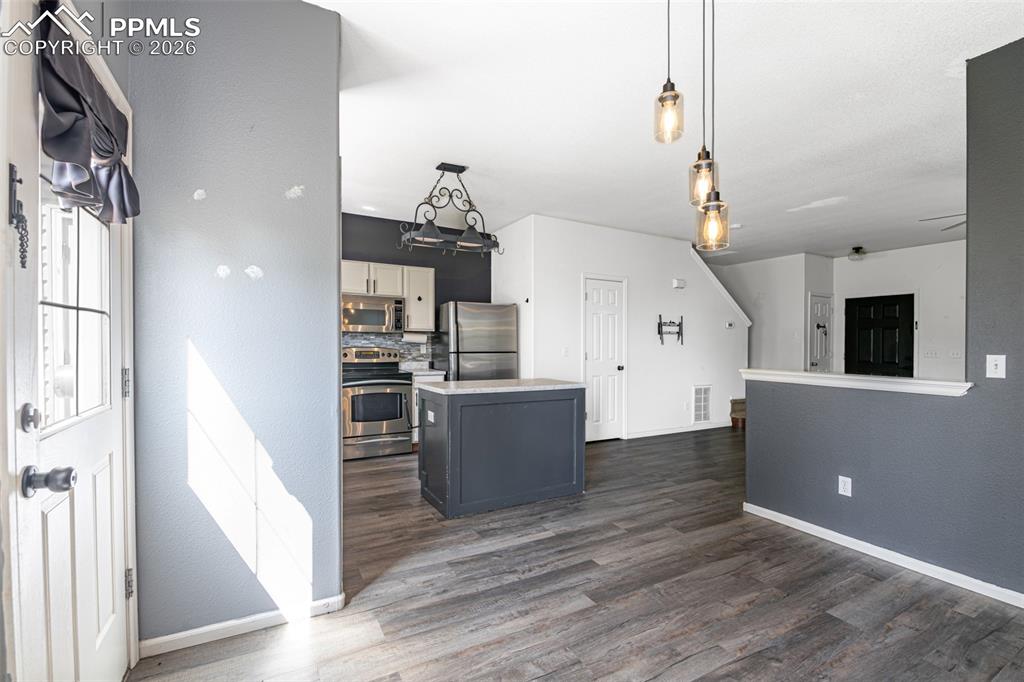 Kitchen with stainless steel appliances, dual tone cabinetry, pendant lighting, light countertops, and dark wood finished floors