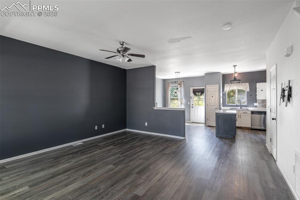 Unfurnished living room featuring an accent wall and ceiling fan and dark wood-style floors