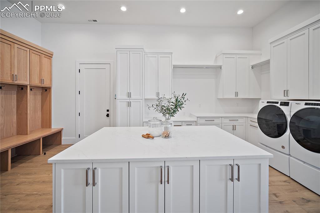 A dream laundry room featuring a fully built-in mudroom, washer and dryer, dedicated tech area, and a center island, all filled with abundant natural light.