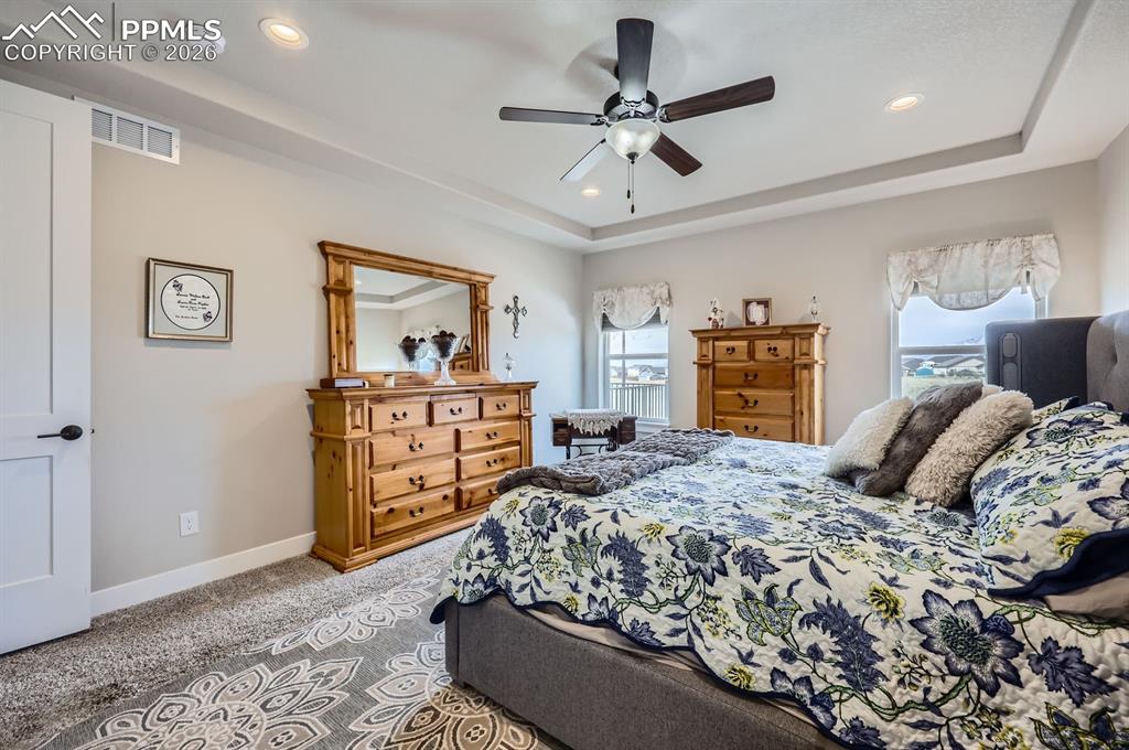 Bedroom with a raised ceiling, carpet flooring, recessed lighting, baseboards, and a ceiling fan
