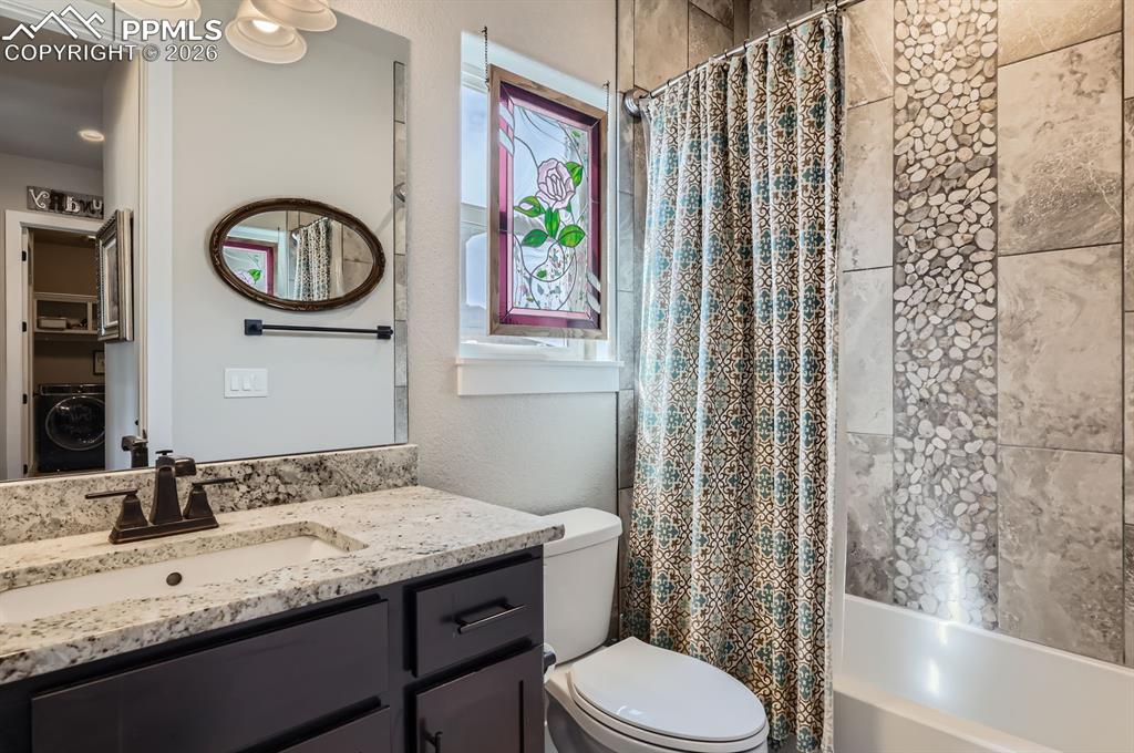 Bathroom with washer / dryer, toilet, shower / bath combo with shower curtain, and vanity