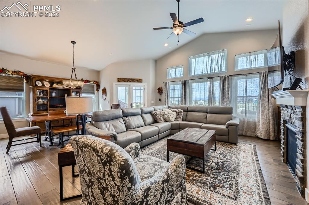 Living room featuring lofted ceiling, hardwood / wood-style flooring, ceiling fan, a stone fireplace, and recessed lighting