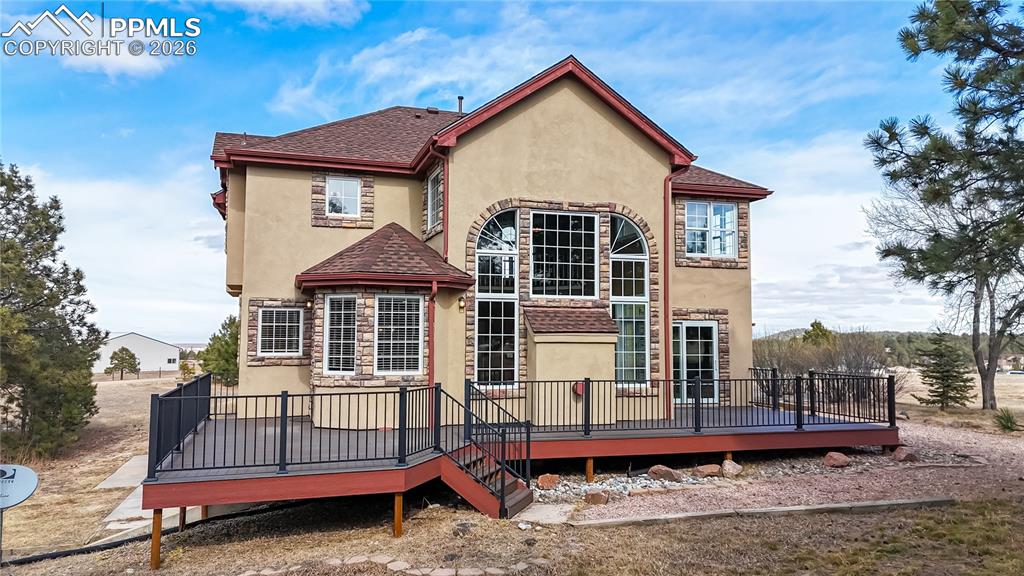 Back of property featuring a wooden deck, stucco siding, and roof with shingles
