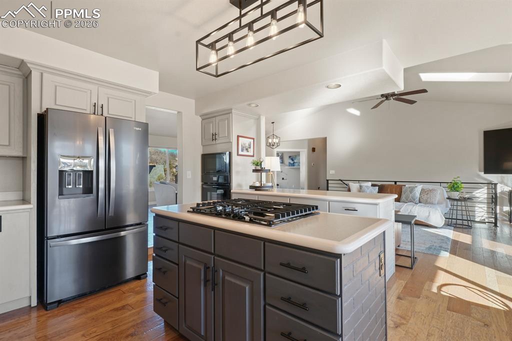 Kitchen with gray cabinetry, appliances with stainless steel finishes, vaulted ceiling with skylight, ceiling fan, and a kitchen island