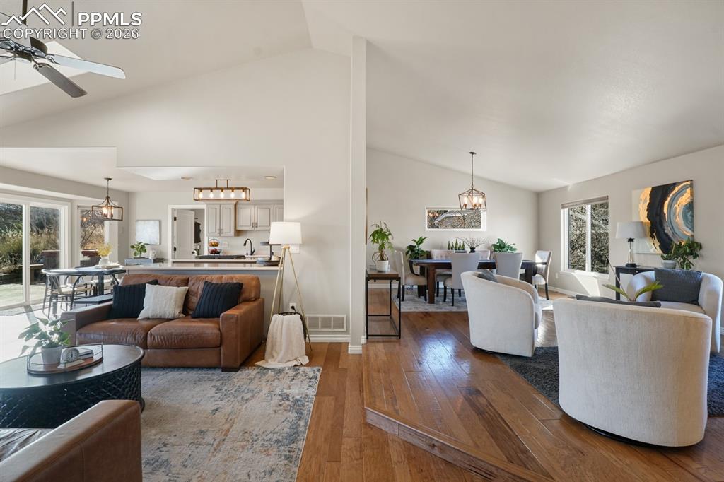 Living room with ceiling fan with notable chandelier, high vaulted ceiling, and hardwood / wood-style floors
