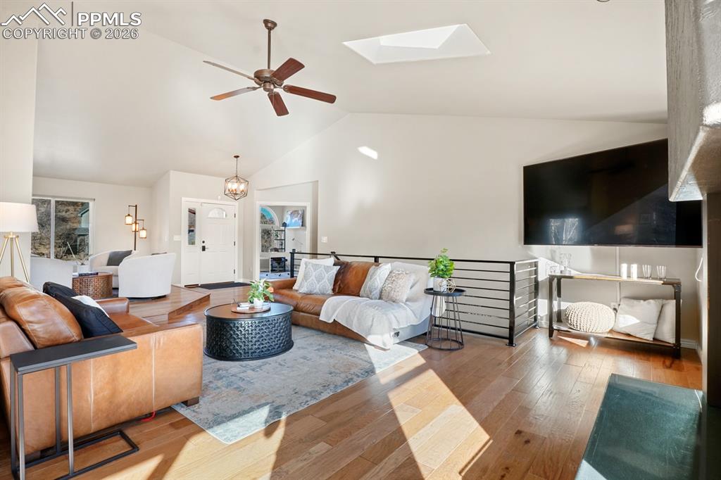 Living room with hardwood / wood-style flooring, high vaulted ceiling, a skylight, and ceiling fan