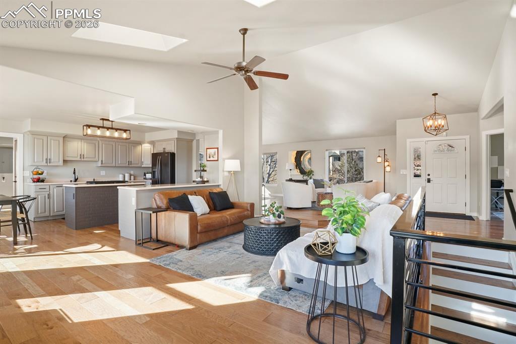 Living room featuring high vaulted ceiling, a skylight, ceiling fan with notable chandelier, and light hardwood / wood-style flooring