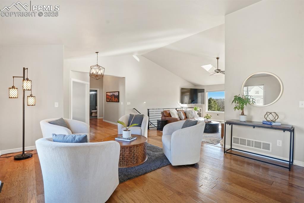 Living room with ceiling fan with notable chandelier, high vaulted ceiling, and hardwood / wood-style flooring