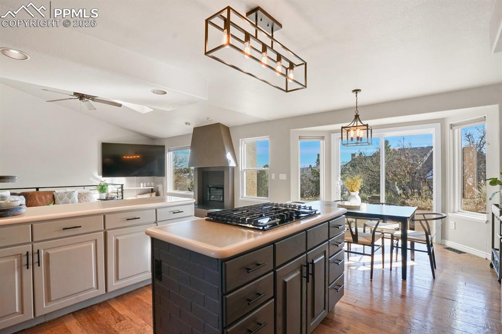 Kitchen featuring ceiling fan with notable chandelier, stainless steel gas cooktop, a kitchen island, lofted ceiling, and light hardwood / wood-style floors