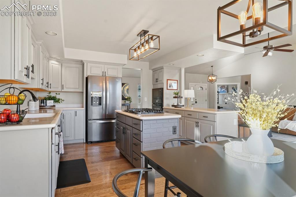 Kitchen with gray cabinets, stainless steel appliances, wood-type flooring, a kitchen island, and hanging light fixtures